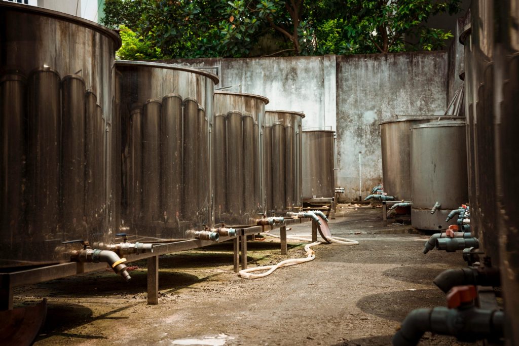 Outdoor view of large industrial metal tanks with connected pipes and concrete surroundings.