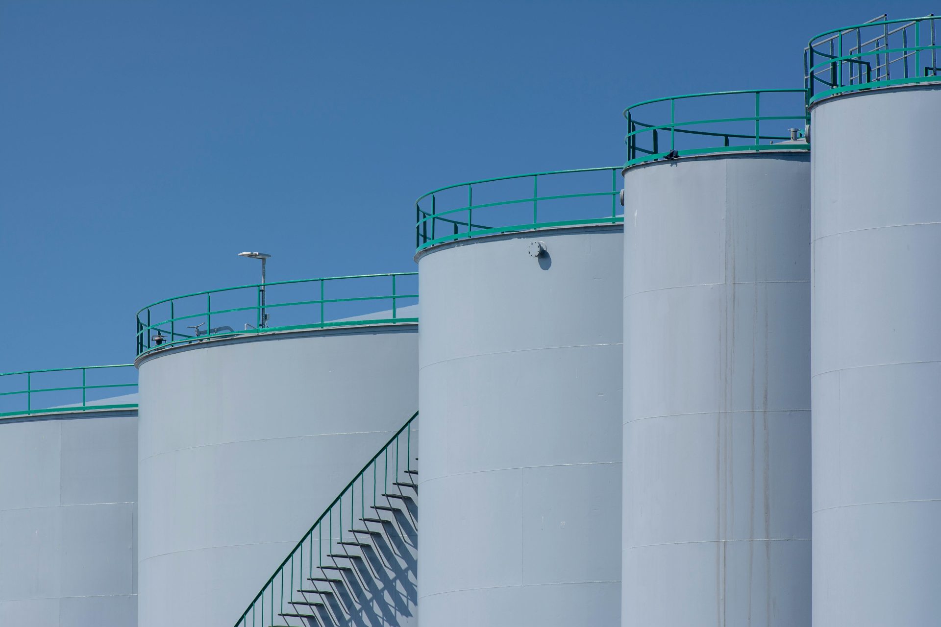 Large industrial storage tanks with green railings against a clear blue sky.