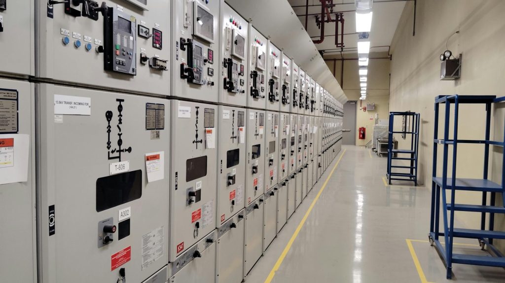 Long row of control panels in an industrial electrical control room, well-lit and spacious.